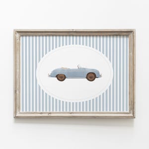 Pu&ograve; includere: Stampa incorniciata con un'illustrazione di un'auto cabriolet azzurra. L'auto &egrave; ambientata su un ovale bianco, con uno sfondo a strisce verticali blu e bianche. La cornice &egrave; di colore marrone chiaro.