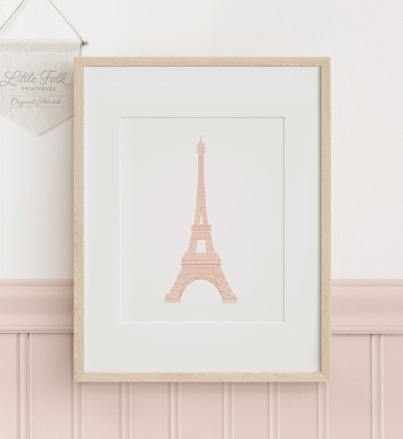 May include: A printable art print featuring a pink outline of the Eiffel Tower on a white background. The print is framed in a light wood frame.