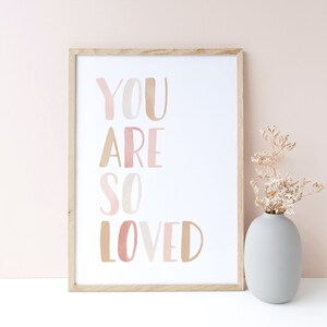 K&ouml;nnte beinhalten: Ein gerahmter Druck mit dem Text "YOU ARE SO LOVED" in rosa und braunen Aquarellbuchstaben auf wei&szlig;em Hintergrund.