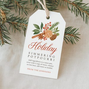 May include: A white rectangular gift tag with a jute string featuring a watercolor illustration of orange slices, cinnamon sticks, pinecones, and berries. The text reads Holiday SIMMERING POTPOURRI, instructions for use, and FROM THE JOHNSONS.