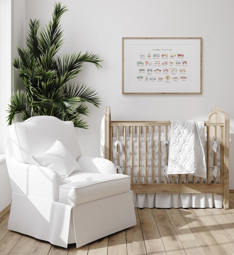 May include: A white cot with a white quilted blanket and a white armchair in a nursery with a framed print that says "Things That Go" with illustrations of various vehicles.