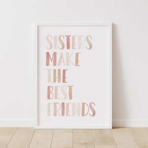 Może przedstawiać: Biały wydruk w ramie z tekstem "Sisters make the best friends" w różowych i brązowych literach akwarelowych.