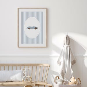 Pu&ograve; includere: Una stampa incorniciata con un'illustrazione di un'auto cabriolet azzurra all'interno di un ovale, su uno sfondo a strisce verticali blu e bianche. La cornice in legno completa la morbida tavolozza di colori, adatta all'arredamento della cameretta.