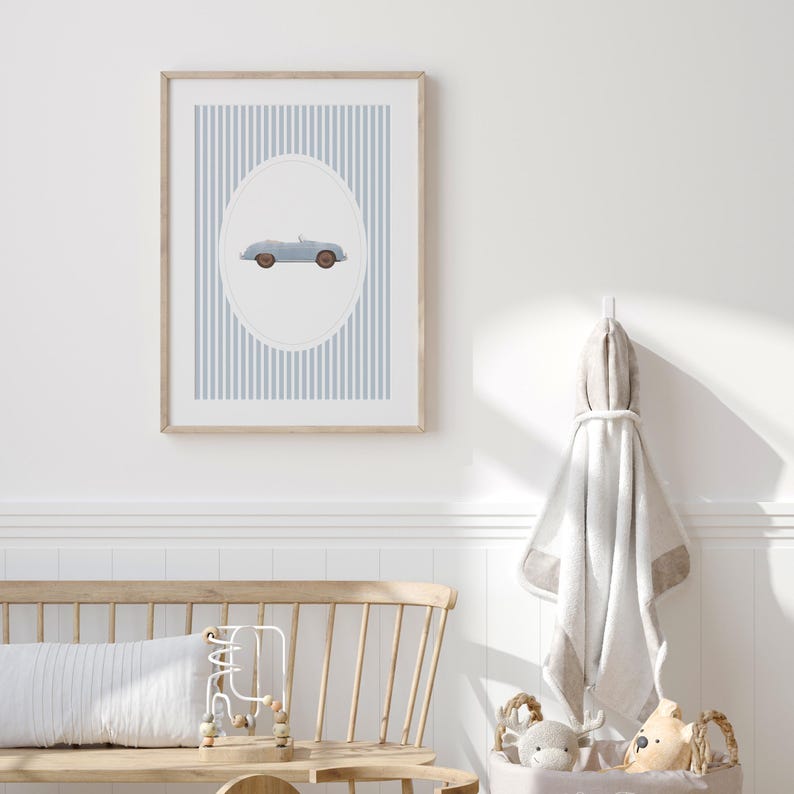 Pu&ograve; includere: Una stampa incorniciata con un'illustrazione di un'auto cabriolet azzurra all'interno di un ovale, su uno sfondo a strisce verticali blu e bianche. La cornice in legno completa la morbida tavolozza di colori, adatta all'arredamento della cameretta.