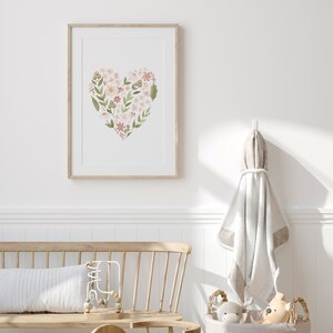 May include: A framed print of a floral heart design in shades of pink, green, and brown. The print is hanging on a white wall in a nursery setting.