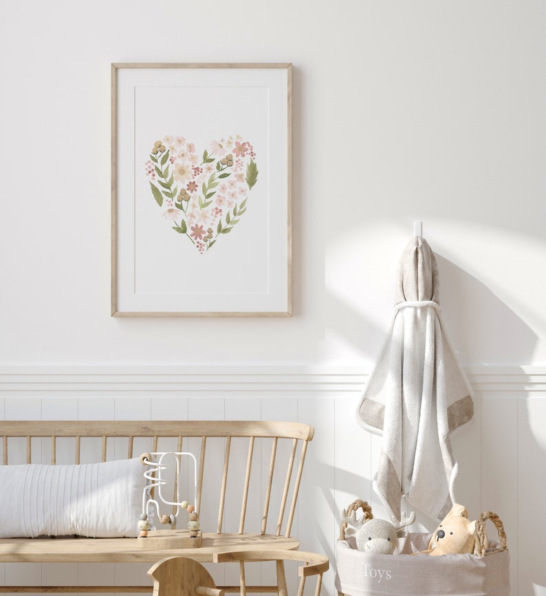 May include: A framed print of a floral heart design in shades of pink, green, and brown. The print is hanging on a white wall in a nursery setting.