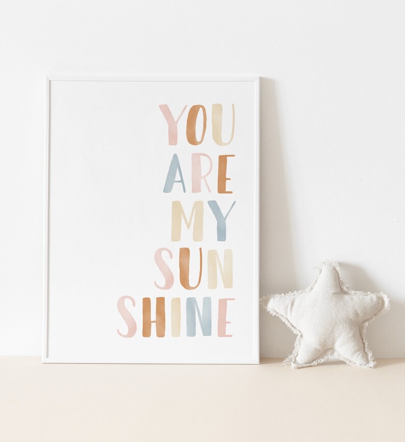 May include: A white framed print with the text "You are my sunshine" in colorful watercolor letters. The letters are in shades of pink, orange, blue, and yellow.