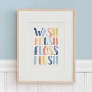 May include: A framed print with the words "WASH BRUSH FLOSS FLUSH" in colorful, watercolor-style lettering. The print is on a white background and has a light wood frame.