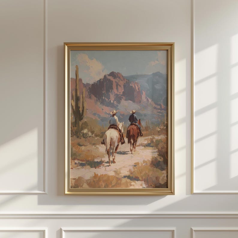 May include: A framed landscape painting depicts two figures on horseback riding through a desert canyon. The artwork features a color palette of muted browns, blues, and greens, with a gold frame.