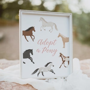 May include: White framed sign with the text "adopt a pony" in pink script. The sign features five cartoon ponies in various colours and poses.
