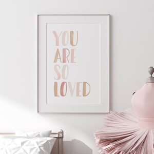 K&ouml;nnte beinhalten: Ein gerahmter Druck mit dem Text "YOU ARE SO LOVED" in Aquarell-Stil mit Ros&eacute;t&ouml;nen und Gold.