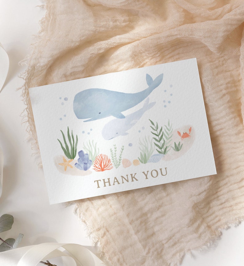 May include: A thank you card with a watercolor illustration of a whale and a baby whale swimming in the ocean. The card has a blue, green, and orange color scheme and features coral, seaweed, and seashells. The text "THANK YOU" is printed in brown at the bottom of the card.
