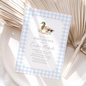 May include: A blue and white gingham baby shower invitation with a watercolor illustration of a duck. The invitation reads "Kindly join us for a Baby Shower in honor of Caroline Michaels. Saturday, August 11, 2024, 2 o'clock in the afternoon, Westview Country Club, 432 Henderson Dr. Aubrey, TX 76543. Kindly RSVP by September 1st, Text Jocelyn at 321.4567, Registered at Baby Boutique."