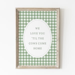May include: Framed wall art with a green and white gingham pattern background. An oval in the center contains the text "WE LOVE YOU 'TIL THE COWS COME HOME" in a simple, elegant font. The frame is a light brown color.