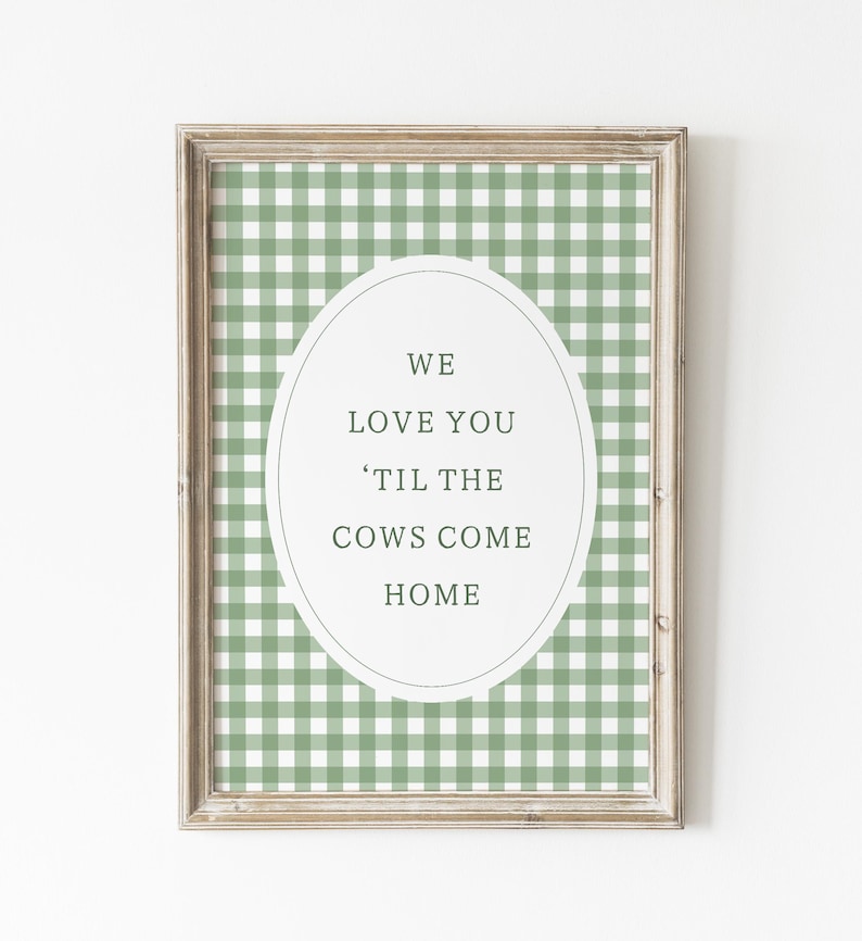 May include: Framed wall art with a green and white gingham pattern background. An oval in the center contains the text "WE LOVE YOU 'TIL THE COWS COME HOME" in a simple, elegant font. The frame is a light brown color.