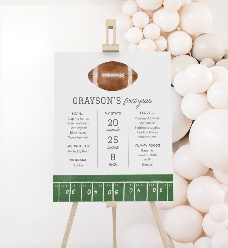 May include: A green and white football-themed first birthday sign with the name Grayson. The sign includes details about the child's first year, such as weight, height, favorite toy, and favorite foods. The sign is decorated with a football and a green and white football field.