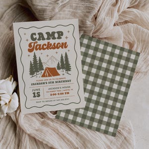 May include: A rectangular birthday invitation card with a wavy border, featuring a camping scene with pine trees, a tent, and mountains. The text reads CAMP JACKSON, JACKSON'S 5TH BIRTHDAY, JUNE 15, 2:00-4:00 PM, and address details. Includes a matching green gingham card.