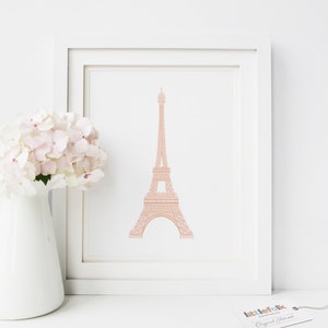 May include: A printable art print featuring a pink outline of the Eiffel Tower on a white background. The print is framed in a white frame and is sitting on a white surface. The print is from the company "littlefolk printables" and says "Original Artwork" at the bottom.