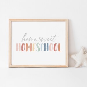 May include: A framed print with the text "home sweet HOMESCHOOL" in a rainbow of colors. The print is in a light wood frame and is sitting on a white surface.
