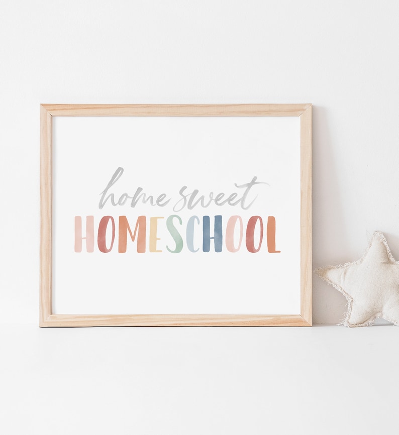 May include: A framed print with the text "home sweet HOMESCHOOL" in a rainbow of colors. The print is in a light wood frame and is sitting on a white surface.