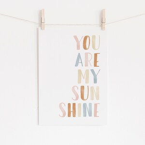 May include: A watercolor print with the text "YOU ARE MY SUNSHINE" in pastel pink, brown, blue, and yellow colors.