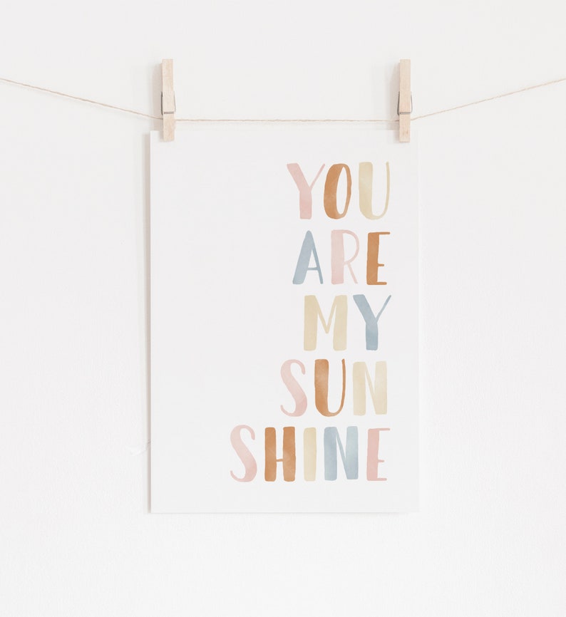 May include: A watercolor print with the text "YOU ARE MY SUNSHINE" in pastel pink, brown, blue, and yellow colors.