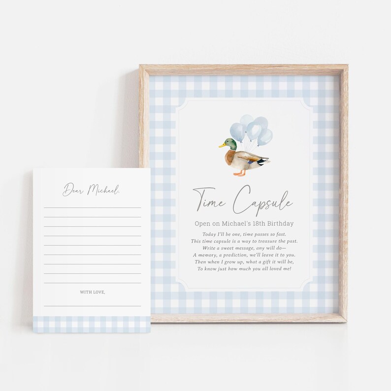 Puede incluir: Un marco con una impresi&oacute;n de c&aacute;psula del tiempo y una tarjeta a juego. La impresi&oacute;n presenta un pato de acuarela con globos y un patr&oacute;n de cuadros vichy azul y blanco. El texto dice "Time Capsule".