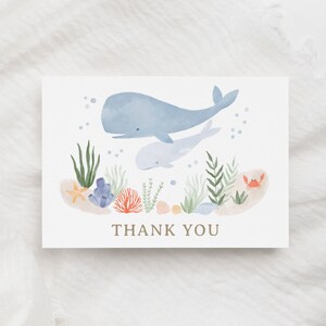 May include: A watercolor thank you card with a blue whale and a baby whale swimming in the ocean. The card features coral, seaweed, seashells, and a crab.