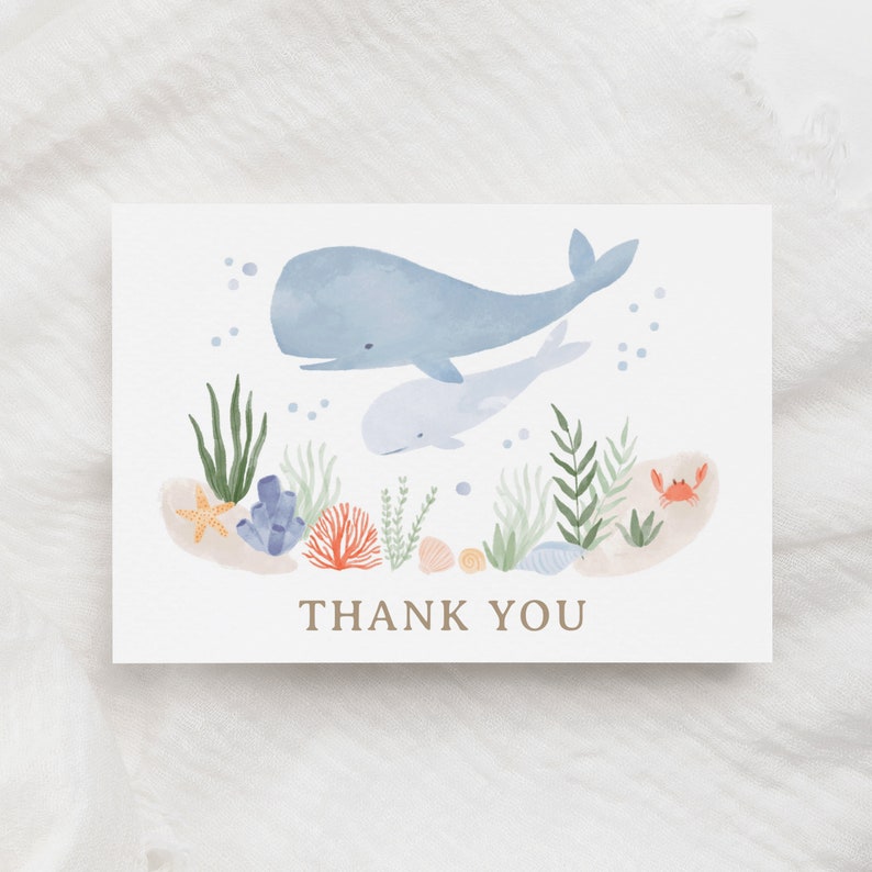 May include: A watercolor thank you card with a blue whale and a baby whale swimming in the ocean. The card features coral, seaweed, seashells, and a crab.