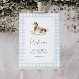 May include: A baby shower welcome sign featuring a watercolor illustration of a duck. The sign has a light blue gingham border and includes the text "Welcome to Caroline's Baby Shower" and the date August 21, 2025.