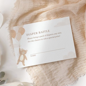May include: A white card with brown text that says "Diaper Raffle" and "Please bring a pack of diapers, any size, For the chance to win a special prize!" There is a brown teddy bear holding balloons and a line for a name.