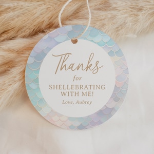 May include: Round, white thank you tag with a blue and purple mermaid scale pattern border. The tag says "Thanks for celebrating with me! Love, Aubrey".