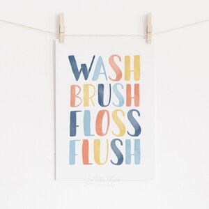 May include: A watercolor print with the words "Wash, Brush, Floss, Flush" in a colorful rainbow pattern. The words are in a stacked vertical format. The print is on a white background and has a subtle watercolor texture.