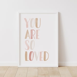 K&ouml;nnte beinhalten: Wei&szlig;er gerahmter Druck mit dem Text "YOU ARE SO LOVED" in rosa und braunen Aquarellbuchstaben.