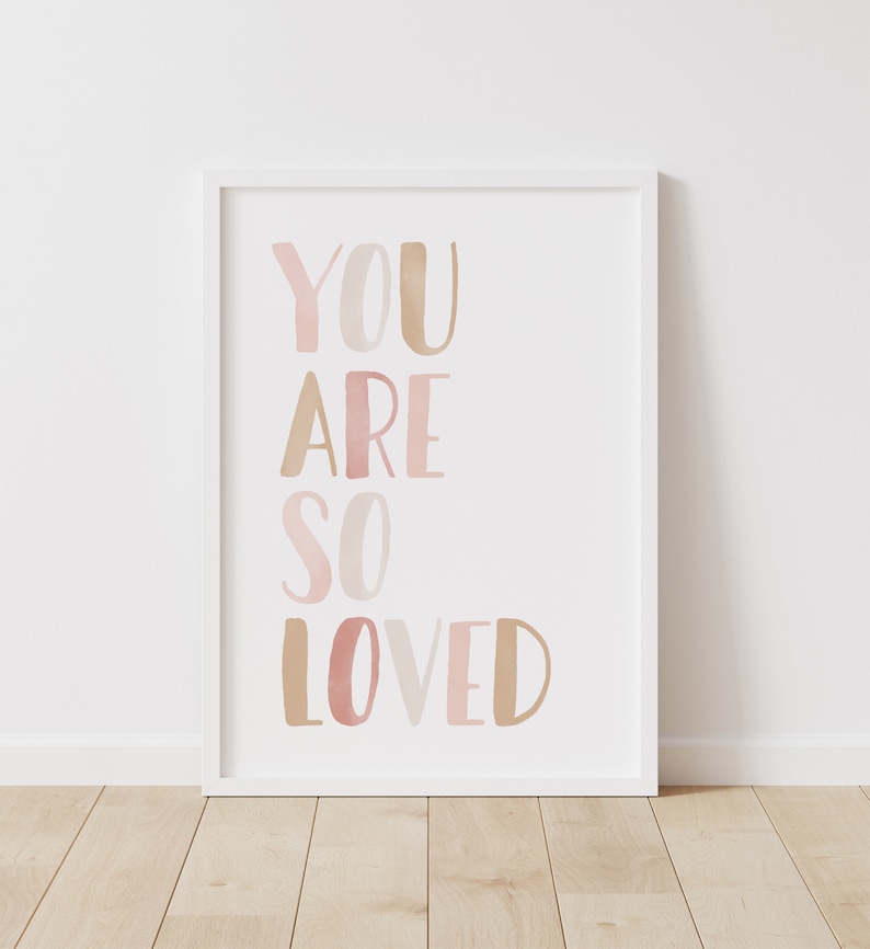 K&ouml;nnte beinhalten: Wei&szlig;er gerahmter Druck mit dem Text "YOU ARE SO LOVED" in rosa und braunen Aquarellbuchstaben.
