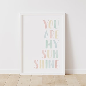 May include: A white framed print with the text "You are my sunshine" in pastel colors. The text is arranged vertically with each word in a different color.