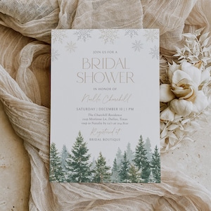 May include: A bridal shower invitation with a winter theme. The invitation features a light beige background with gold text and snowflake accents. A watercolor forest scene is at the bottom. The text reads "Join us for a Bridal Shower".