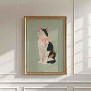 Puede incluir: Impresión artística enmarcada de un gato calicó con un lazo rosa. El gato está representado sentado con los ojos cerrados, sobre un fondo verde claro. El marco dorado añade un toque de elegancia a la obra.