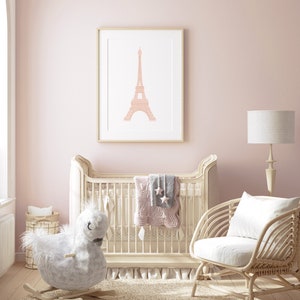 May include: A white crib with a pink and gray quilt and a rocking horse toy. A wicker chair with a white cushion sits next to the crib. A framed print of the Eiffel Tower hangs on the wall.