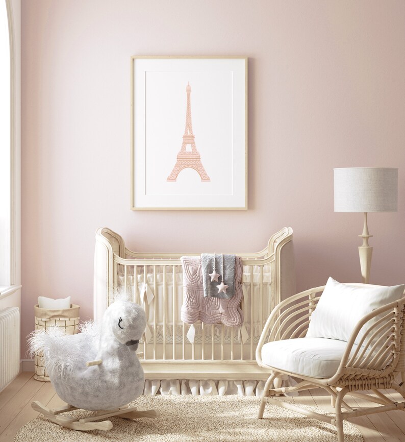 May include: A white crib with a pink and gray quilt and a rocking horse toy. A wicker chair with a white cushion sits next to the crib. A framed print of the Eiffel Tower hangs on the wall.