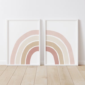 Op de afbeelding: Twee ingelijste prints van abstracte regenbogen in tinten roze, beige en bruin. De prints zijn in witte lijsten en hangen aan een witte muur.