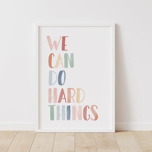 Peut inclure: Une impression encadrée blanche avec le texte "WE CAN DO HARD THINGS" en lettres colorées de style aquarelle.