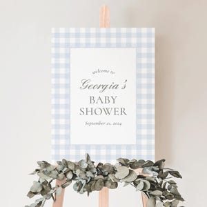 K&ouml;nnte beinhalten: Ein blaues und wei&szlig;es Gingham-Willkommenszeichen f&uuml;r eine Babyparty. Das Schild lautet "Willkommen zur Babyparty von Georgia, 21. September 2024".