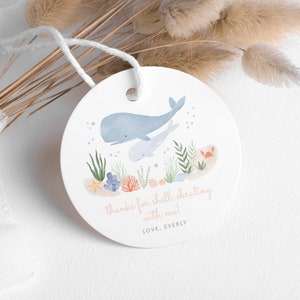 Puede incluir: Una etiqueta redonda blanca con una ballena azul y una ballena más pequeña nadando en un océano azul con coral, algas y un cangrejo. La etiqueta dice "thanks for shell-ebrating with me! LOVE, EVERLY"