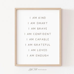 Może przedstawiać: Oprawiony wydruk z białym tłem i czarnym tekstem. Tekst brzmi: „I AM KIND, I AM SMART, I AM BRAVE, I AM CONFIDENT, I AM CAPABLE, I AM GRATEFUL, I AM LOVED, I AM ENOUGH.” Rama jest w kolorze jasnobrązowym. Słowa „Little Folk Printables” znajdują się na dole.