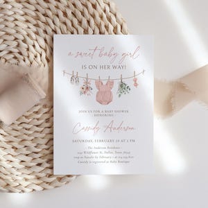 May include: A pink baby shower invitation with a watercolor illustration of baby clothes hanging on a clothesline. The text reads "a sweet baby girl is on her way!" and includes the name "Cassidy Anderson" and details for the baby shower.