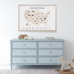 Puede incluir: Una c&oacute;moda azul claro con seis cajones y pomos de madera. La c&oacute;moda est&aacute; en una habitaci&oacute;n con una pared blanca y una alfombra en el suelo. Un mapa enmarcado de los Estados Unidos con el texto "National Parks of the United States" est&aacute; colgado en la pared sobre la c&oacute;moda. Un autob&uacute;s de juguete de madera y un coche est&aacute;n encima de la c&oacute;moda. Un caballo de balanc&iacute;n de madera est&aacute; en la alfombra delante de la c&oacute;moda.