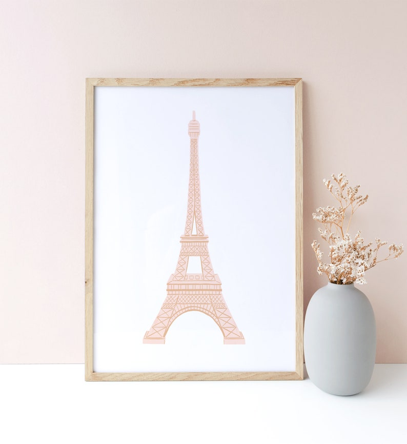 May include: A framed print of a pink outline of the Eiffel Tower on a white background. The frame is light wood and the print is sitting on a white surface.