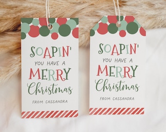 Op de afbeelding: Twee kerstcadeaulabels met de tekst "SOAPIN' YOU HAVE A MERRY Christmas FROM CASSANDRA". De labels hebben een witte achtergrond met rode en groene stippen en een rood-witte gestreepte onderkant.