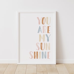 May include: A white framed print with the text "YOU ARE MY SUNSHINE" in colorful watercolor letters. The letters are in shades of pink, orange, brown, blue, and yellow.